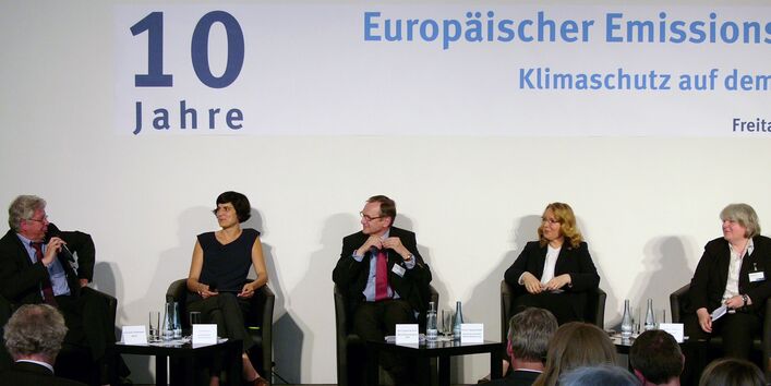drei Frauen und zwei Männer sitzen auf einem Podium und diskutieren. Auf einem Banner darüber steht "10 Jahre Europäischer Emissionshandel"