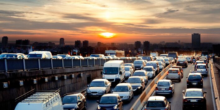 Autos im Stau, im Hintergrund eine Stadt und eine auf- oder untergehende Sonne