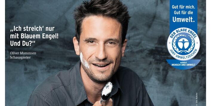 Oliver Mommsen mit einem Pinsel und Farbe im Gesicht und Schriftzug "Ich streich´ nur mit Blauem Engel! Und Du? daneben das Logo "Blauer Engel"