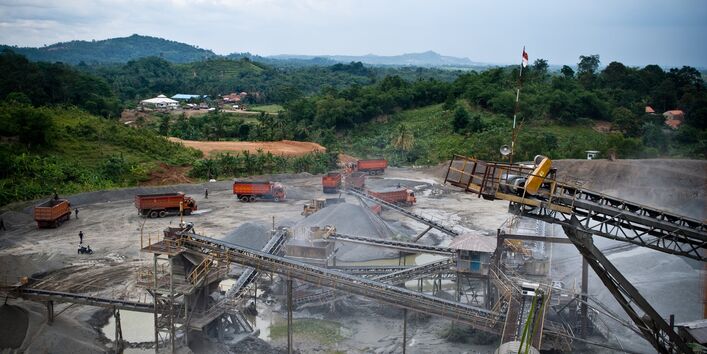 innerhalb einer grünen, hügeligen Landschaft ein kahles, staubiges Areal mit Lkws, Förderbändern und Gesteinshalden