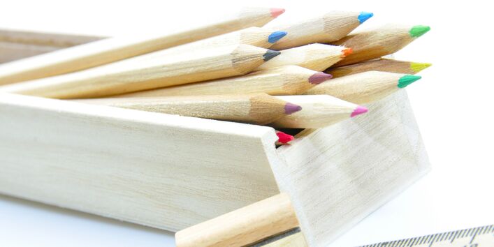 unlackierte Holz-Buntstifte in einem Holzkästchen, daneben ein Anspitzer aus Holz und ein Lineal