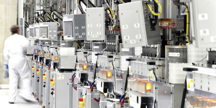 Arbeiter mit weißem Schutzanzug in der Werkhalle einer Chipfabrik mit vielen Geräten