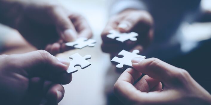 vier Hände halten je ein Puzzlestück in die Mitte