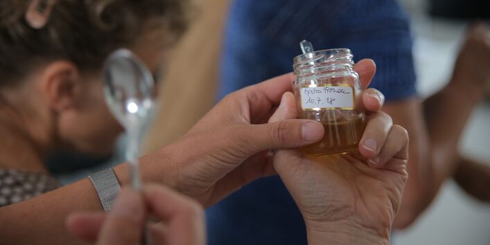 zwei Hände halten ein kleines Glas Honig, das mit dem Datum 10.7.2018 versehen ist.