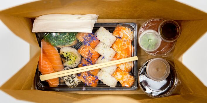 Sushi and several sauces all individually wrapped in disposable plastic containers in a take away paper bag