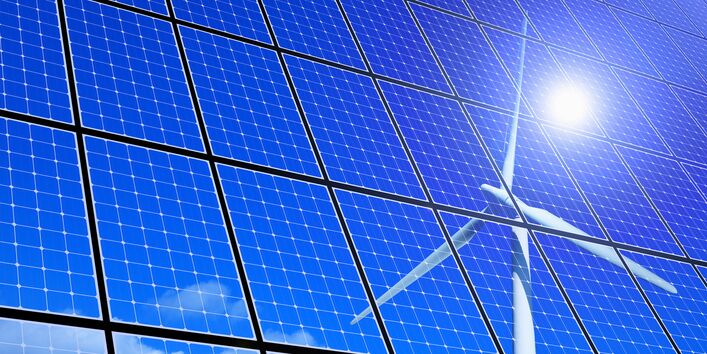 eine Windkraftanlage, die Sonne und Schönwetterwolken an einem blauen Himmel spiegeln sich in Solarzellen