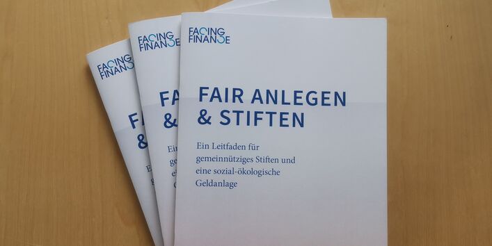 drei Druckversionen des Leitfadens "Fair anlegen & stiften", auf dem Cover sind Windkraftanlagen abgebildet