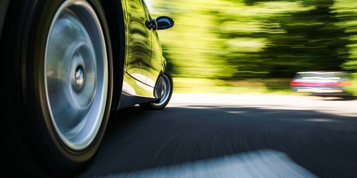 ein Auto fährt über eine Fahrbahn, man sieht den rechten Hinterreifen in Großaufnahme