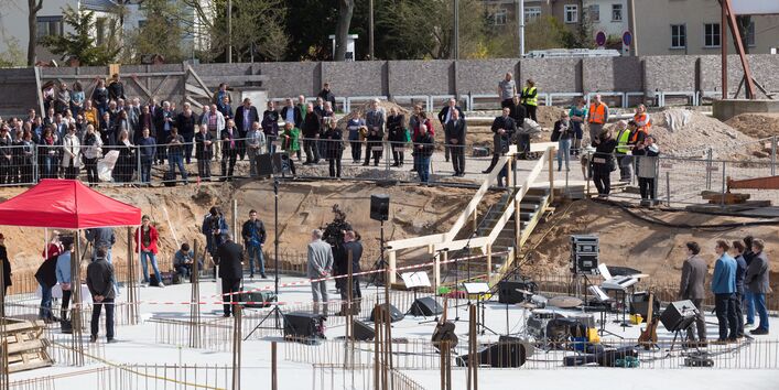 Blick von oben auf eine betonierte Bodenplatte, auf der ein Fest gefeiert wird. Viele Gäste stehen am Rand der Baustelle.