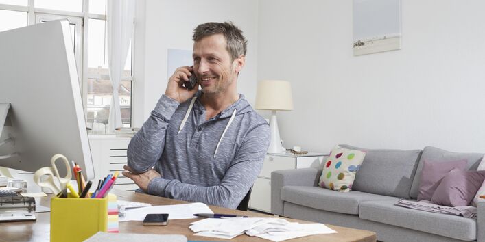 ein Mann sitzt in einem Wohnzimmer am Computer und telefoniert