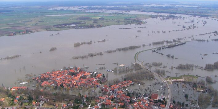 Luftbild: eine Landschaft mit einer Siedlung ist großflächig überschwemmt