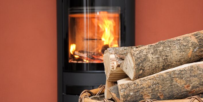 vor einem brennenden Kamin steht ein Korb mit Holzscheiten