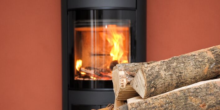 Vor einem brennenden Kaminofen steht ein Korb mit Scheitholz
