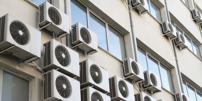 außen an einer Hauswand hängen viele Klimageräte