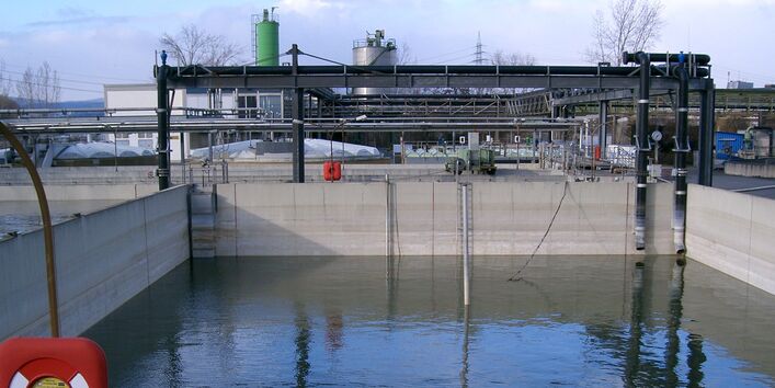 wassergefülltes, quadratisches Betonbecken vor einer Industrieanlage