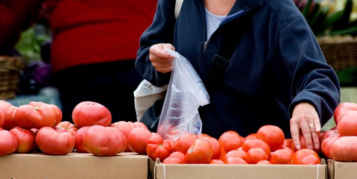 eine Kundin packt an einem Marktstand Tomaten in einen dünnen Plastikbeutel
