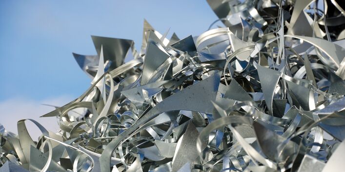Verschnitt-Stücke aus silbernen Metallblechen liegen auf einem großen Haufen, dahinter ist blauer Himmel zu sehen