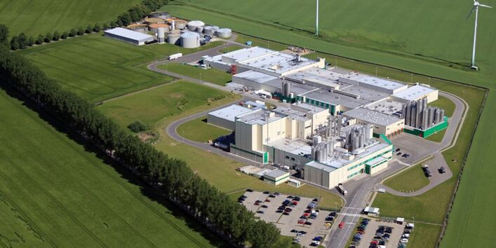 Firmengelände mit mehreren Gebäuden, Tanks und einem Parkplatz inmitten von Feldern