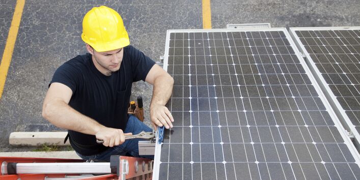 A worker with a hard hat stands on a ladder and installs a photovoltaic system on a roof