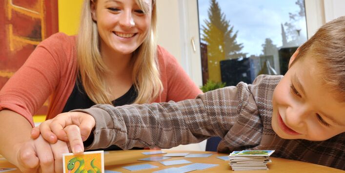 Mutter und Kind beim Memory-Spielen, die Mutter deckt ein Kärtchen mit einer Schlange auf, der Junge schaut neugierig unter die Karte, bevor sie ganz aufgedeckt ist