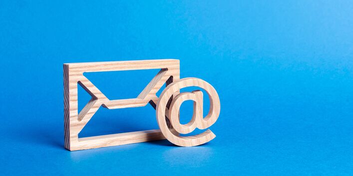 symbolischer Briefumschlag und @-Zeichen aus Holz vor blauem Hintergrund