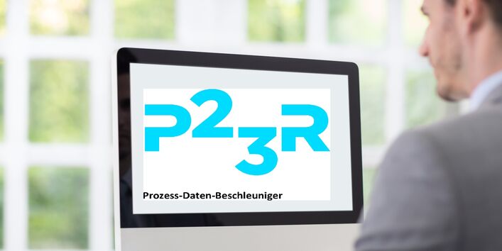 ein junger Mann im Anzug sitzt im Büro an einem Schreibtisch. Auf dem Computermonitor steht "P23R Prozess-Daten-Beschleuniger"