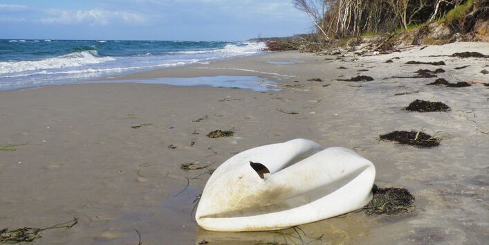 an einem Sansstrand am Meer liegt ein weißer Gegenstand, der einem Schwan ähnelt, aber ein kaputter weißer Gymnastikball oder ein ähnlicher Kunststoffgegenstand ist