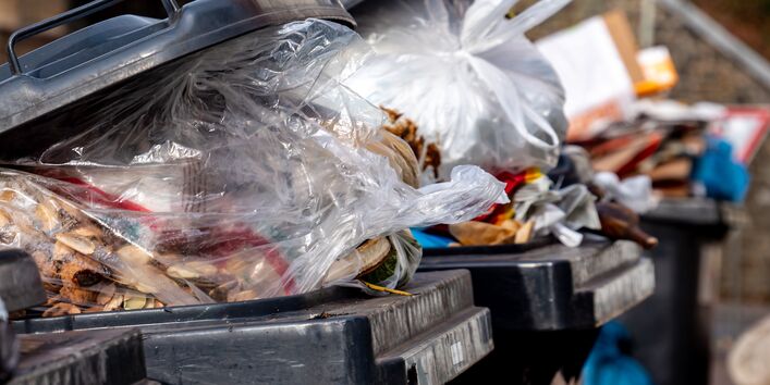 schwarze Tonnen, aus denen Restmüll in Mülltüten herausquillt