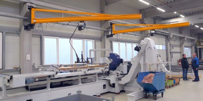 niedrige, aber breite Maschine in einer Werkshalle. Eine Metallstange ist eingespannt, Metallspäne werden in einen Rollcontainer geleitet.