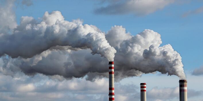 rauchende Industrie-Schornsteine vor einem bewölkten Himmel