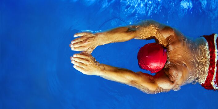 Mann schwimmt in einem Schwimmbecken mit blauem, klaren Wasser. Er trägt eine Badekappe.