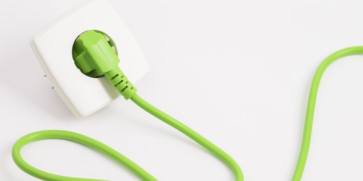 ein grüner Stecker mit grünem Stromkabel steckt in einer Steckdose
