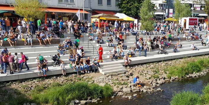 Menschen sitzen auf einer breiten Stufenanlage an einem kleinen Fluss