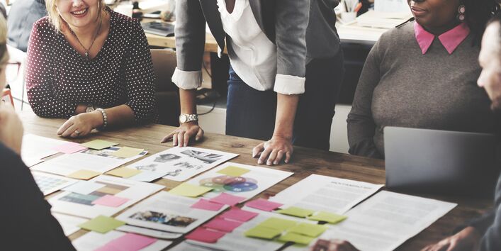 Frauen und Männer sitzen um einen Tisch mit Papierausdrucken und diskutieren 