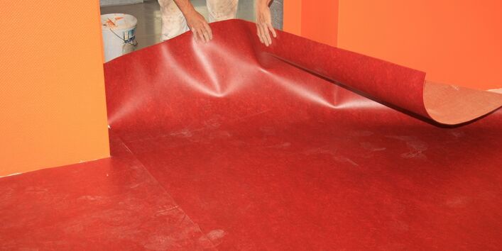 Handwerker verlegt in einer frisch gestrichenen Wohnung einen Fußbodenbelag