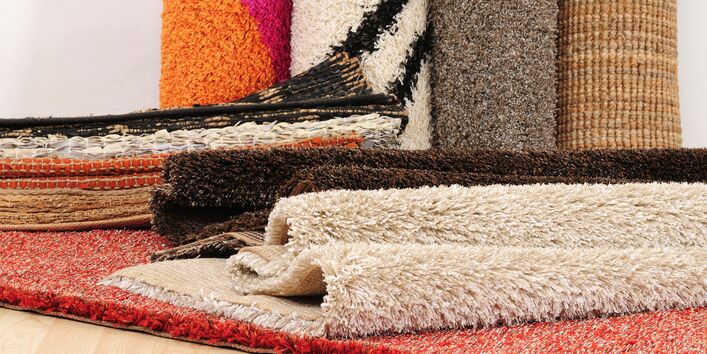 mehrere Teppiche auf einem Haufen, dahinter stehen Teppich-Rollen