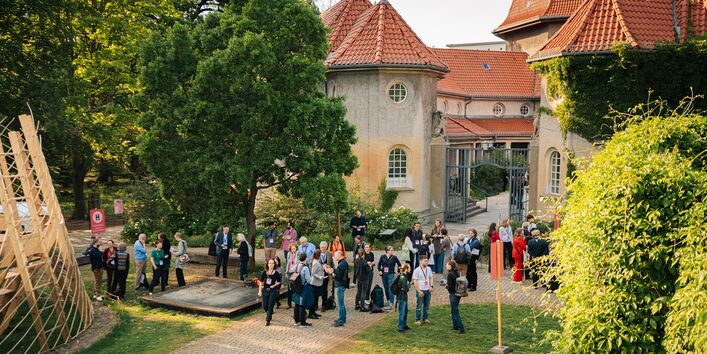 Vor dem ehemaligen Krematorium öffnet sich eine Grünfläche, auf der sich TeilnehmerInnen austauschen.