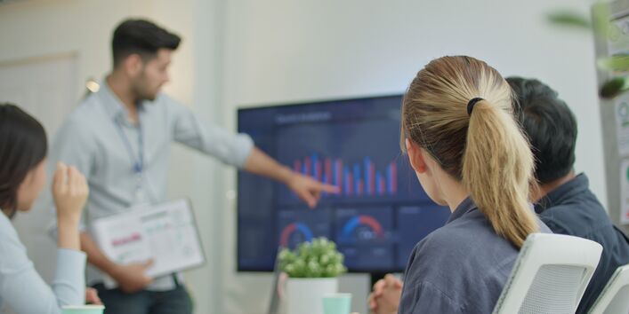 mehrere Personen schauen sich Diagramme auf einem großen Monitor an