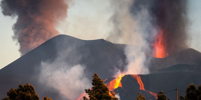 aus einem Vulkan steigen Rauchwolken auf und es fließt glühende Lava hinab