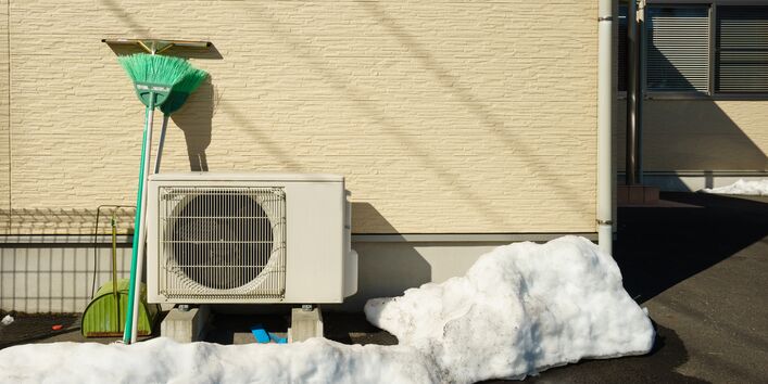 Kasten mit Ventilator an der Außenwand eines Einfamilienhauses, daneben wurde Schnee zusammengekehrt