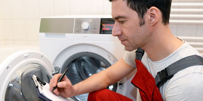 Monteur macht sich Notizen zu einer defekten Waschmaschine