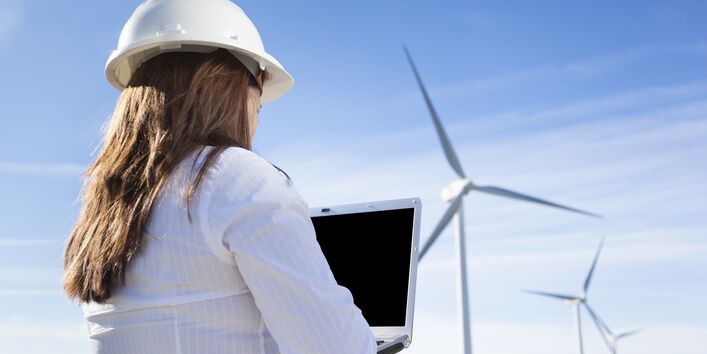 Ingenieurin steht mit Laptop und Bauhelm vor einem Windpark