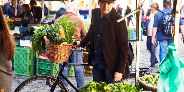 ein Mann kauft mit dem Fahrrad Gemüse auf einem Wochenmarkt ein
