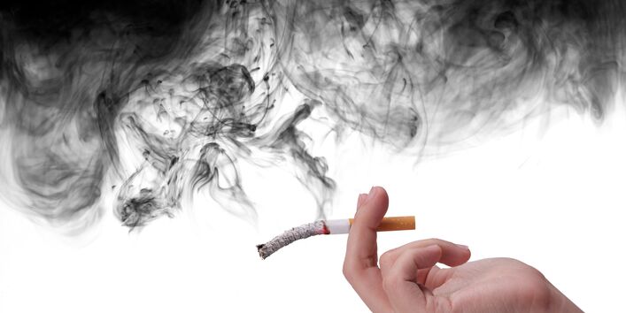 Hand hält eine schon halb zu Asche gewordene Zigarette, von der schwarzer Qualm aufsteigt