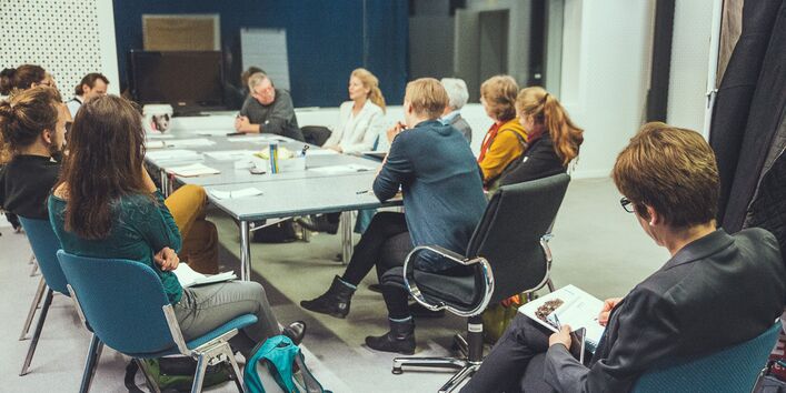 Gruppe von diskutierenden Teilnehmern im Hintergrund, schräg davor eine weitere Person