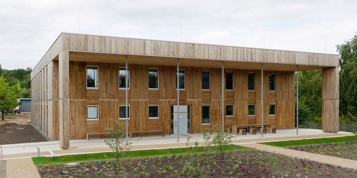 zweistöckiges, quadratisches Haus mit Flachdach und Holzfassade, davor sind Außenanlagen frisch bepflanzt und Wege neu angelegt