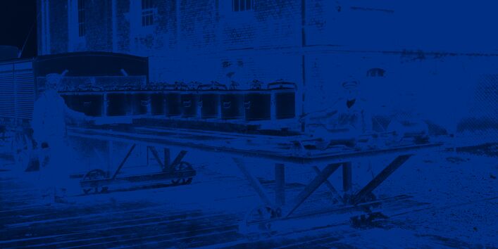 Zwei Männer tauschen Eimer auf einem auf Schienen laufenden Wagen aus.