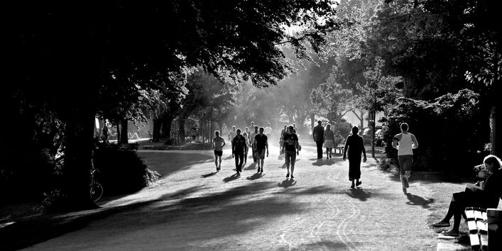 Schwarz-weiß-Aufnahme eines Parks, in dem viele Menschen joggen, spazierengehen oder auf einer Bank sitzen.