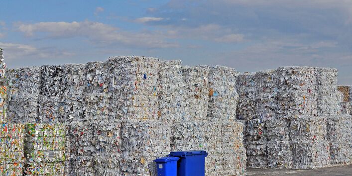 riesige Altpapierstapel und zwei blaue Papiertonnen