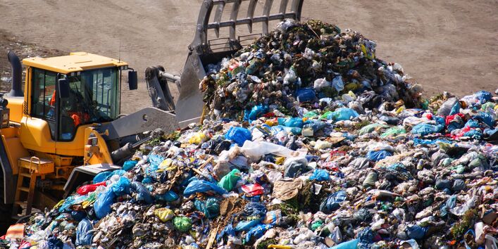 Ein Bagger schiebt den Müll der Abfalldeponie zusammen